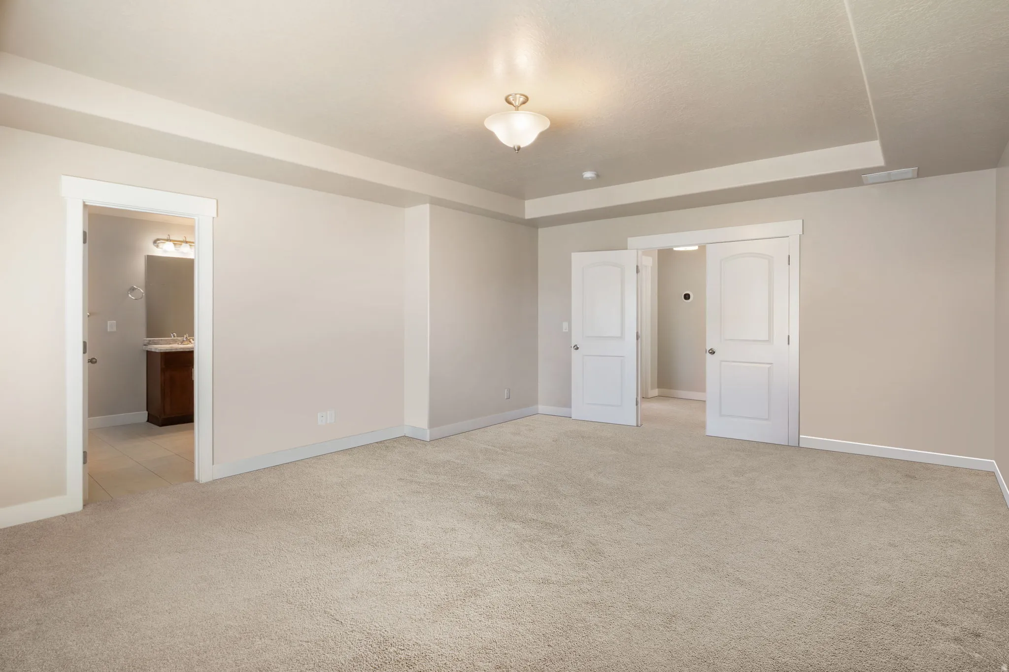 Unfurnished bedroom featuring light colored carpet, a tray ceiling, and ensuite bath