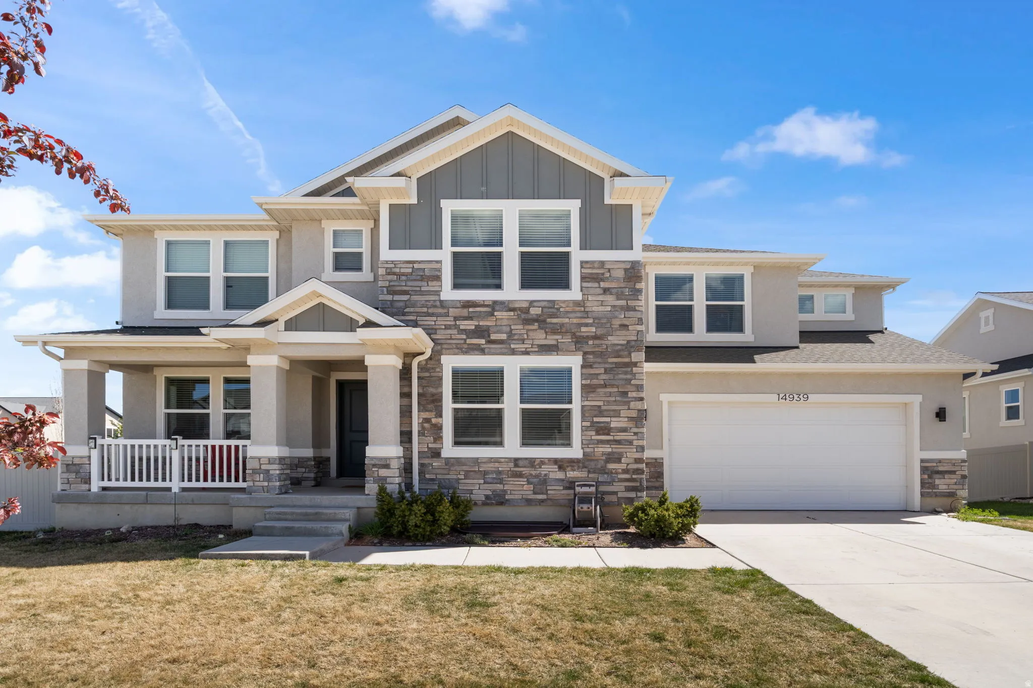 Craftsman house featuring concrete driveway, a front lawn, stone siding, board and batten siding, and covered porch
