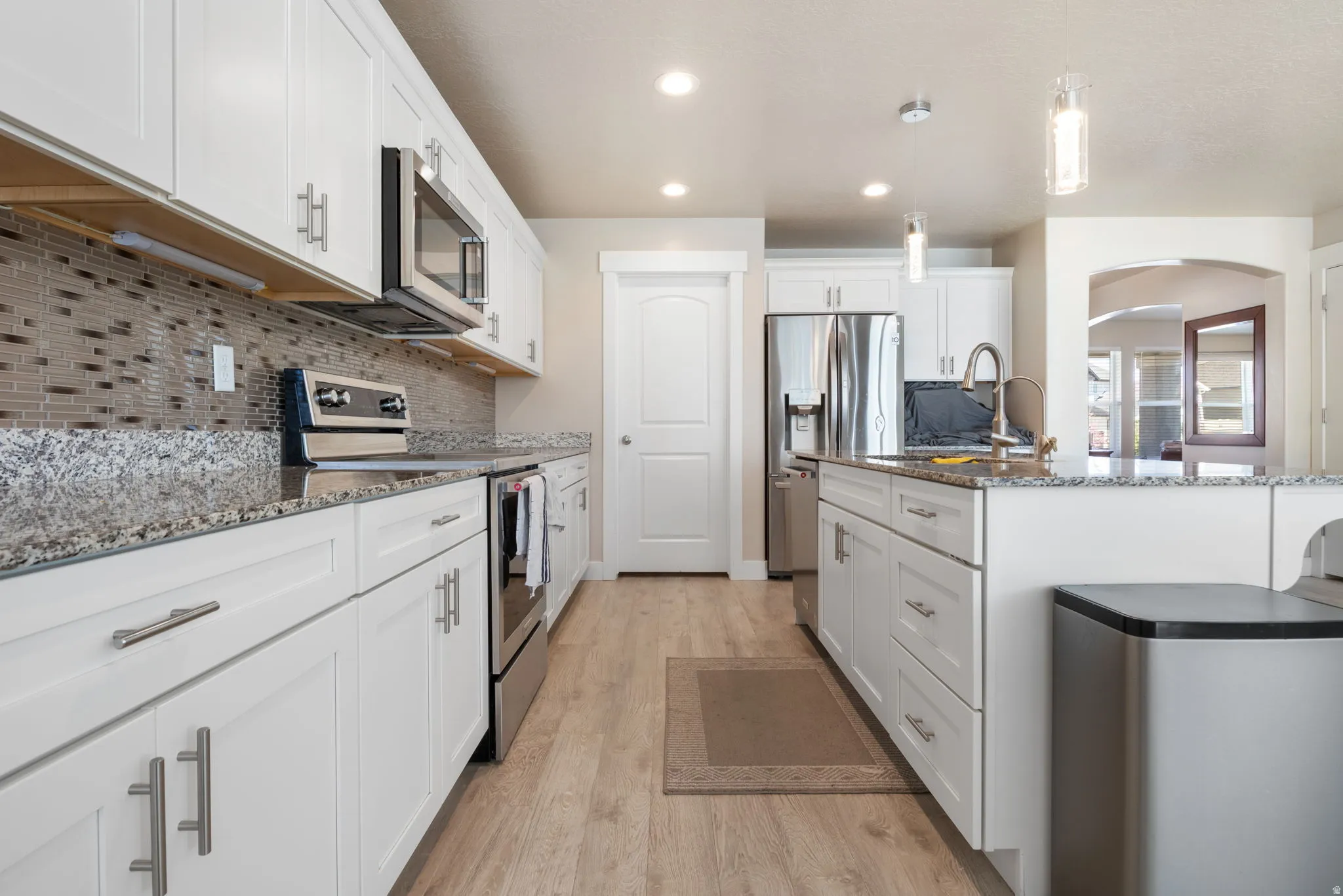 Kitchen featuring stainless steel appliances, white cabinetry, dark stone counters, pendant lighting, and a center island with sink