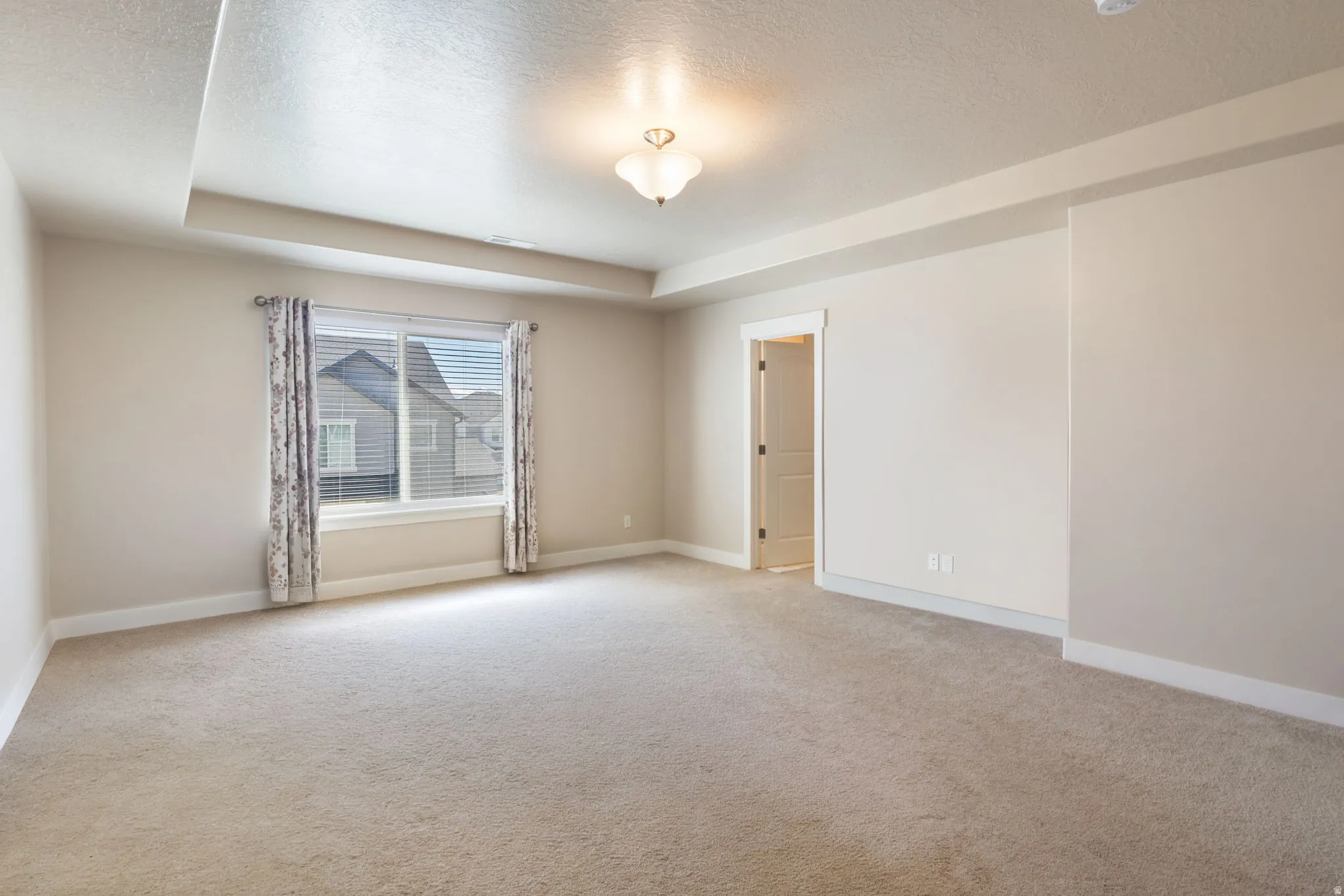 Unfurnished room featuring light carpet, a tray ceiling, and a textured ceiling