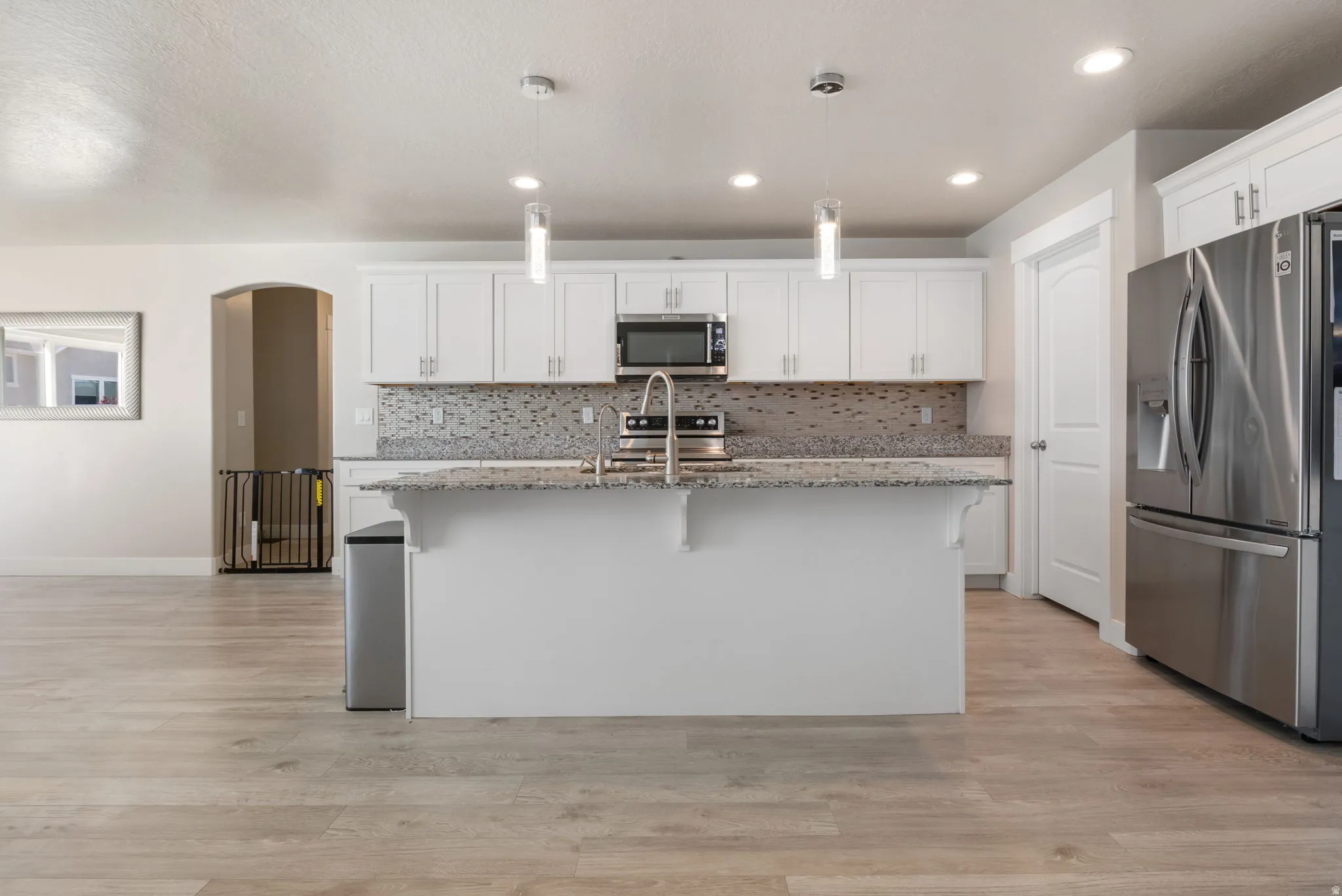 Kitchen with stainless steel appliances, light stone counters, white cabinetry, a kitchen island with sink, and a breakfast bar area