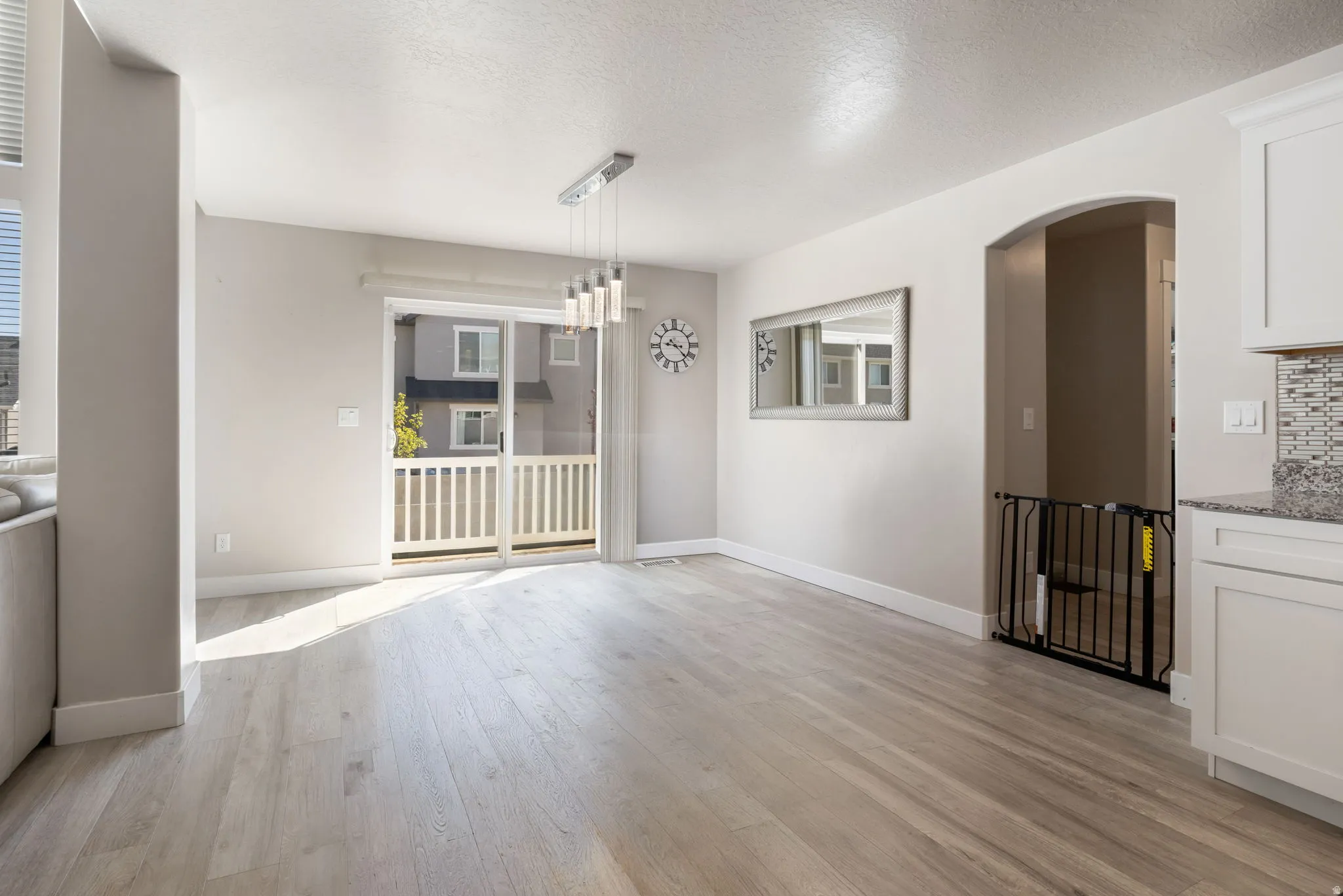 Unfurnished dining area with light wood finished floors, arched walkways, a textured ceiling, and suspended lighting