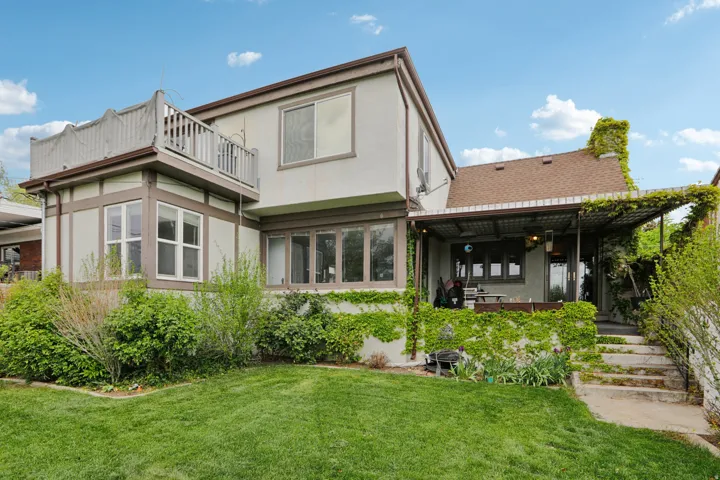 Back of house with stucco siding, a yard, a chimney, and a sunroom