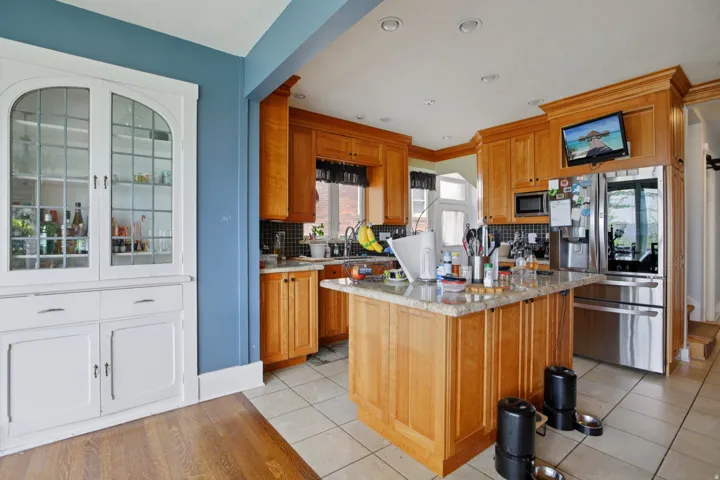 Kitchen featuring stainless steel appliances, light stone countertops, wood finish cabinetry, tasteful backsplash, and a center island