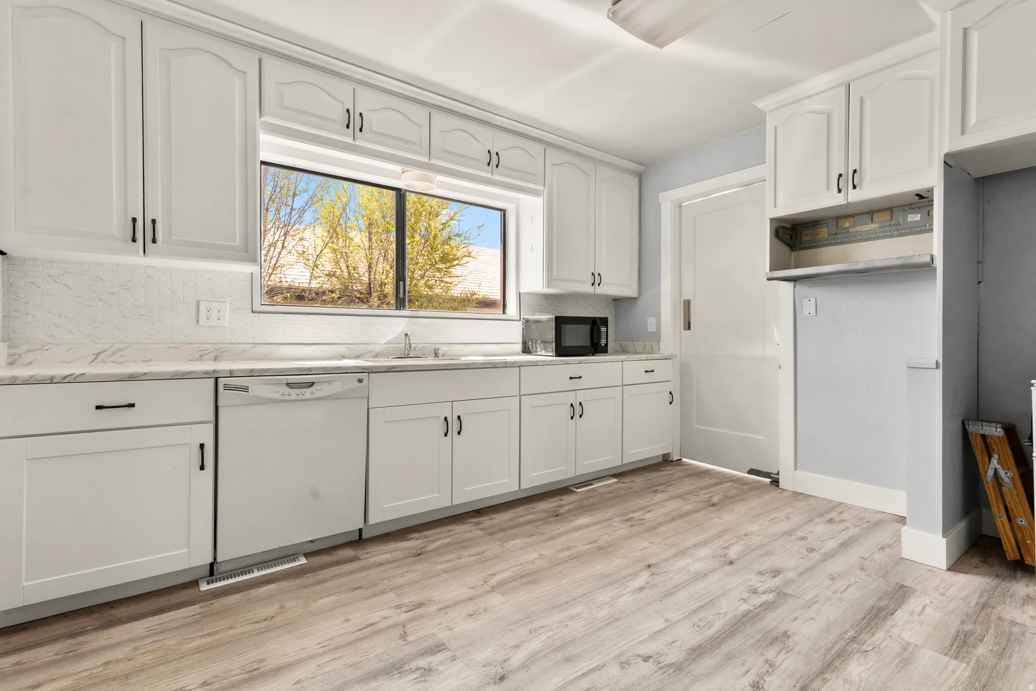 Kitchen featuring white cabinets, dishwasher, black microwave, light wood-style flooring, and light stone countertops