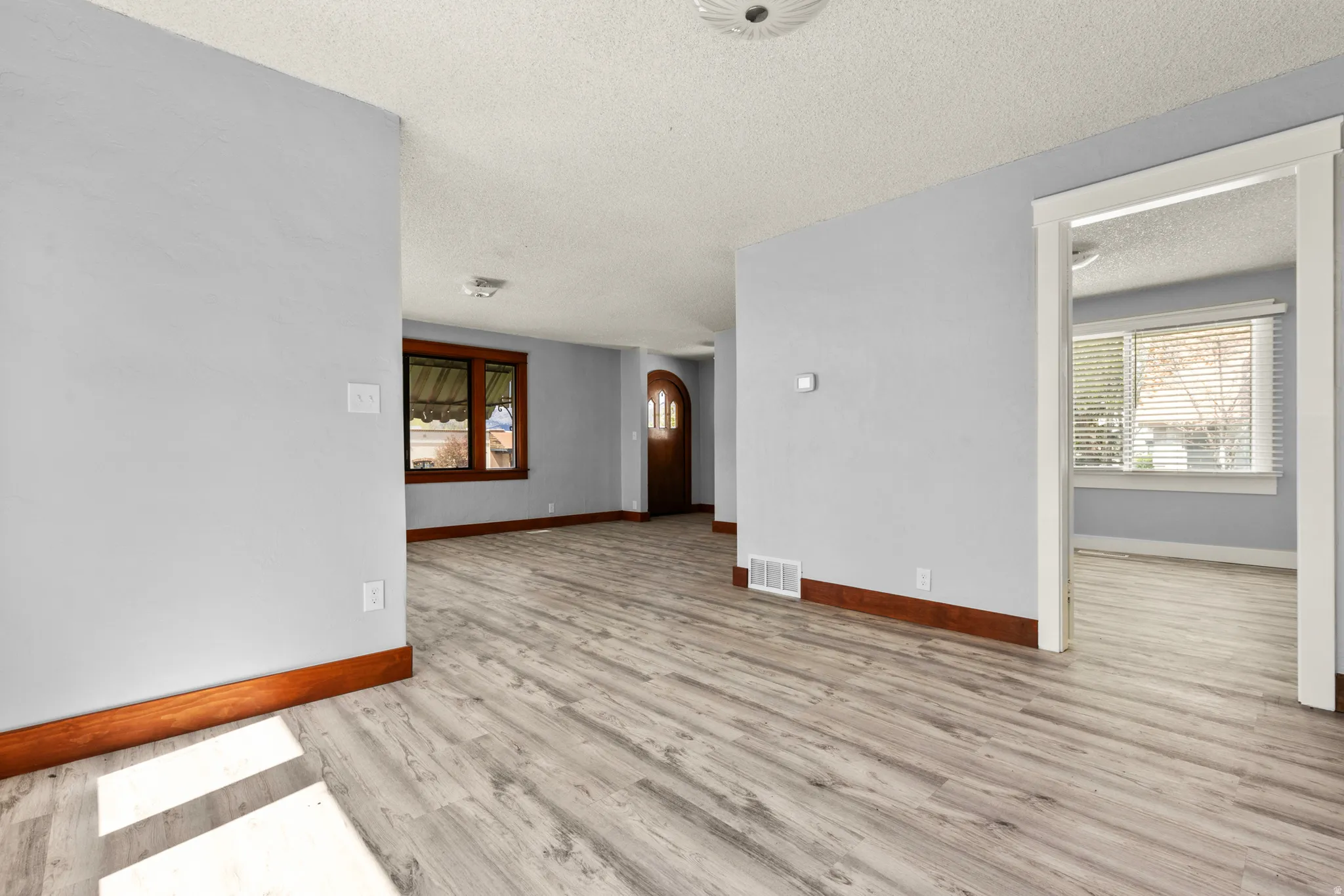 Unfurnished room with arched walkways, light wood-type flooring, and a textured ceiling