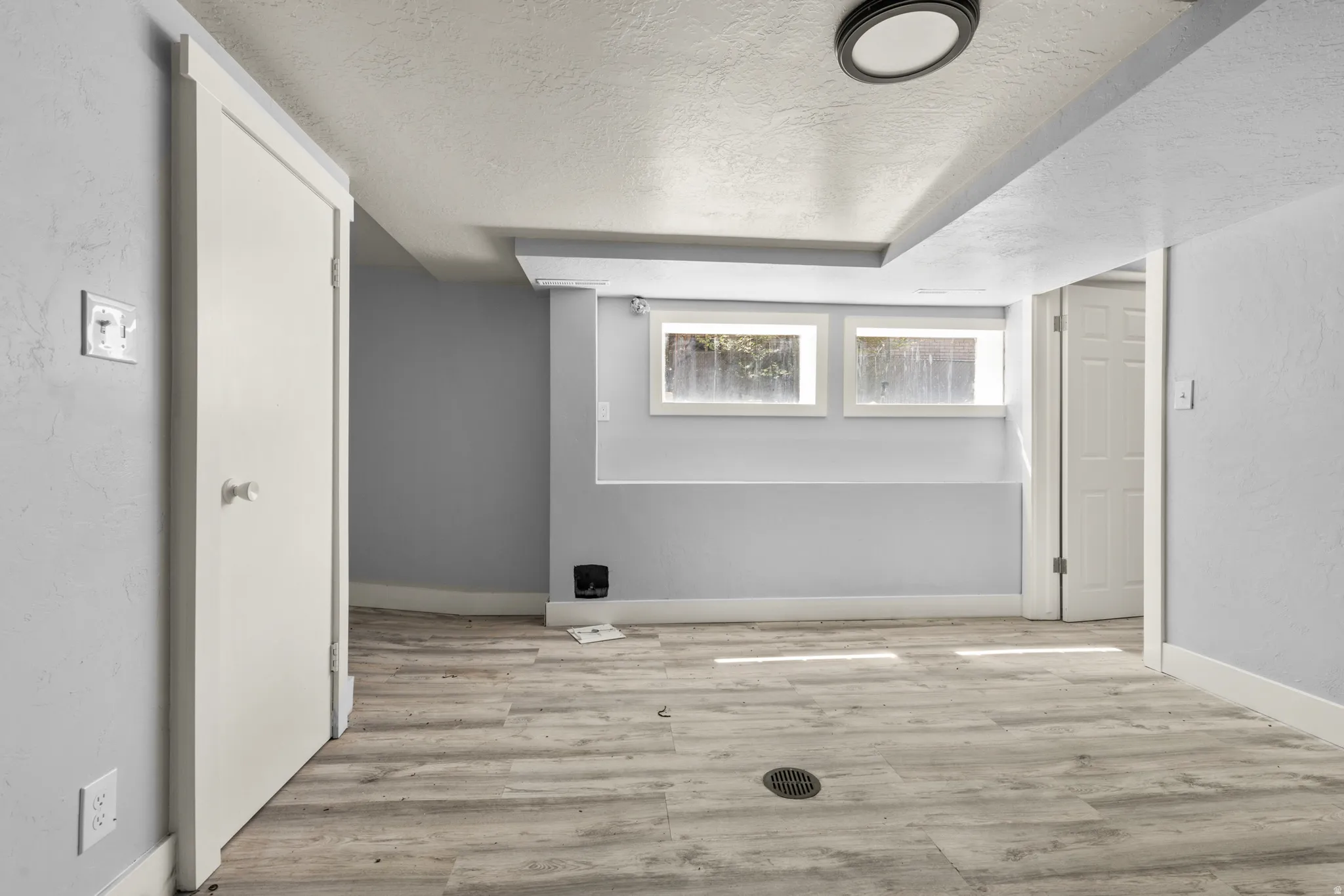 Basement featuring a textured ceiling, light wood finished floors, and a textured wall