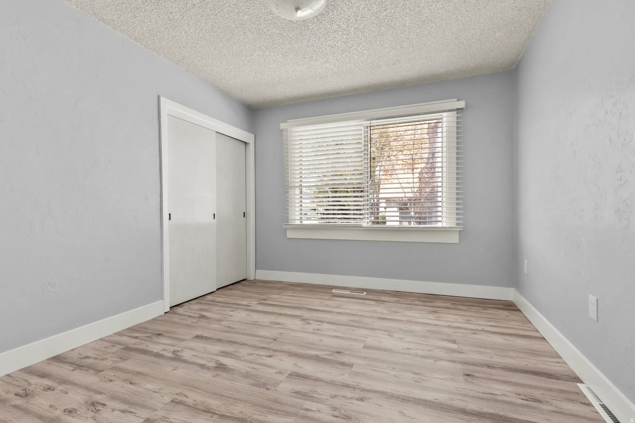 Unfurnished bedroom featuring light wood finished floors, a closet, a textured ceiling, and a textured wall