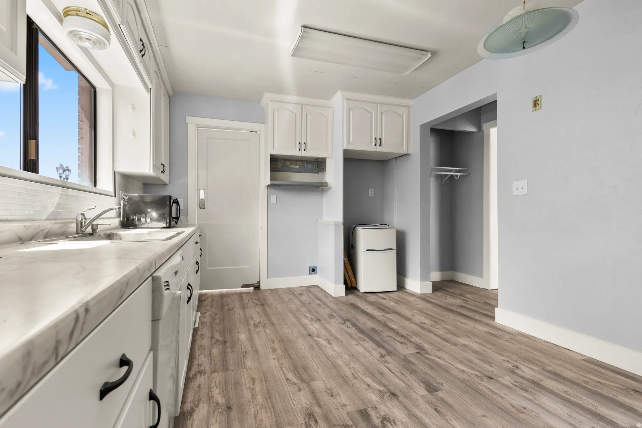 Kitchen with white cabinets, light countertops, light wood-style floors, freestanding refrigerator, and dishwasher