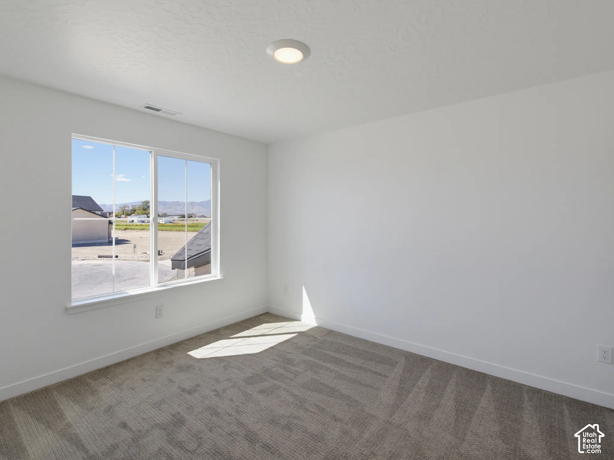 Neutral painted walls, gray carpet, and a large window with white trim, featuring recessed ceiling lighting