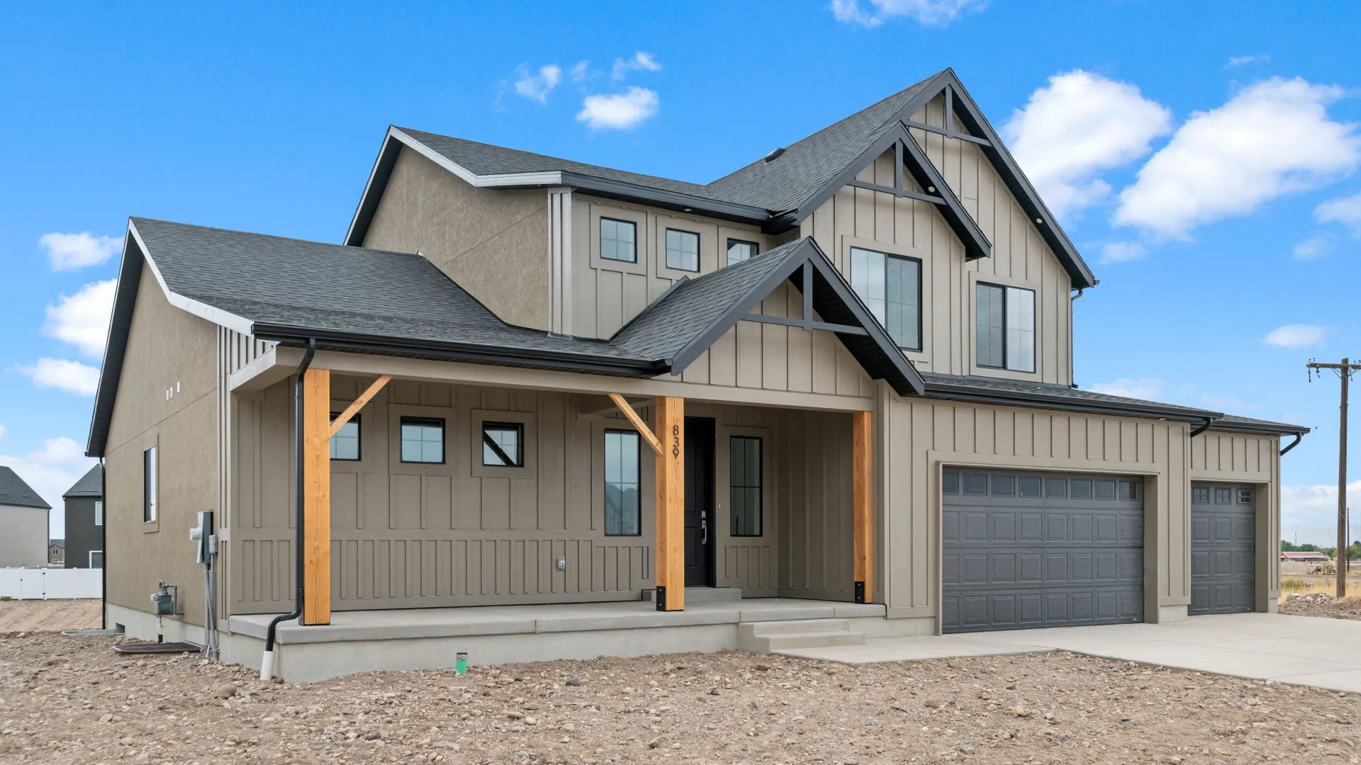 Contemporary farmhouse exterior featuring board-and-batten siding, a covered porch with natural wood posts, a two-car garage, and a single-car garage