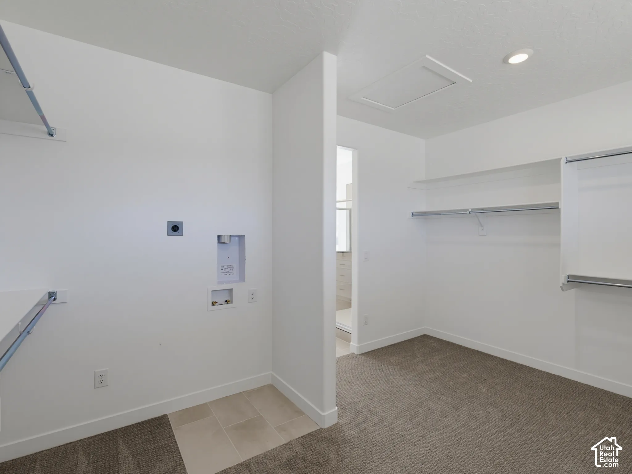 Laundry area with tile flooring and appliance hookups, complemented by carpeted storage space featuring white shelving and metal hanging rods