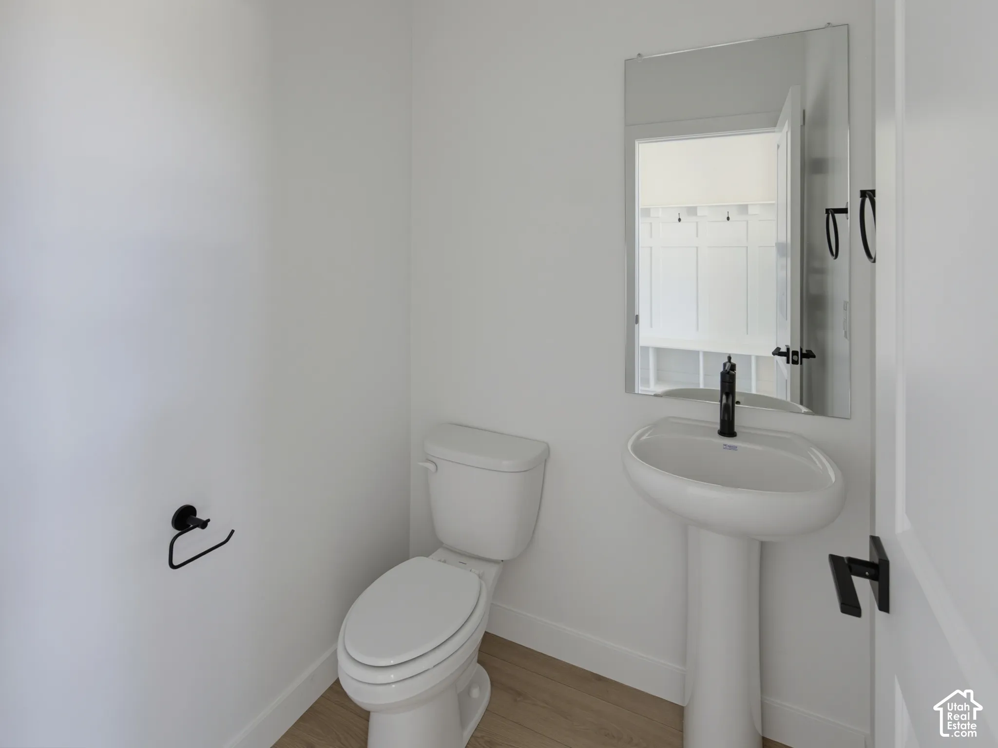 White pedestal sink with a matte black faucet, matching toilet, and wood-finish flooring