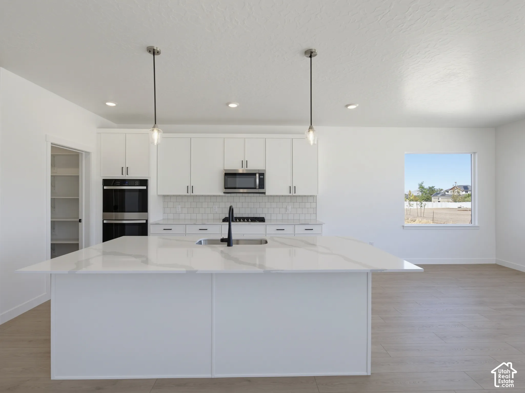 Contemporary kitchen featuring a large island with a light-toned countertop, white cabinetry with dark hardware, a subway tile backsplash, and stainless steel appliances including a double oven and microwave