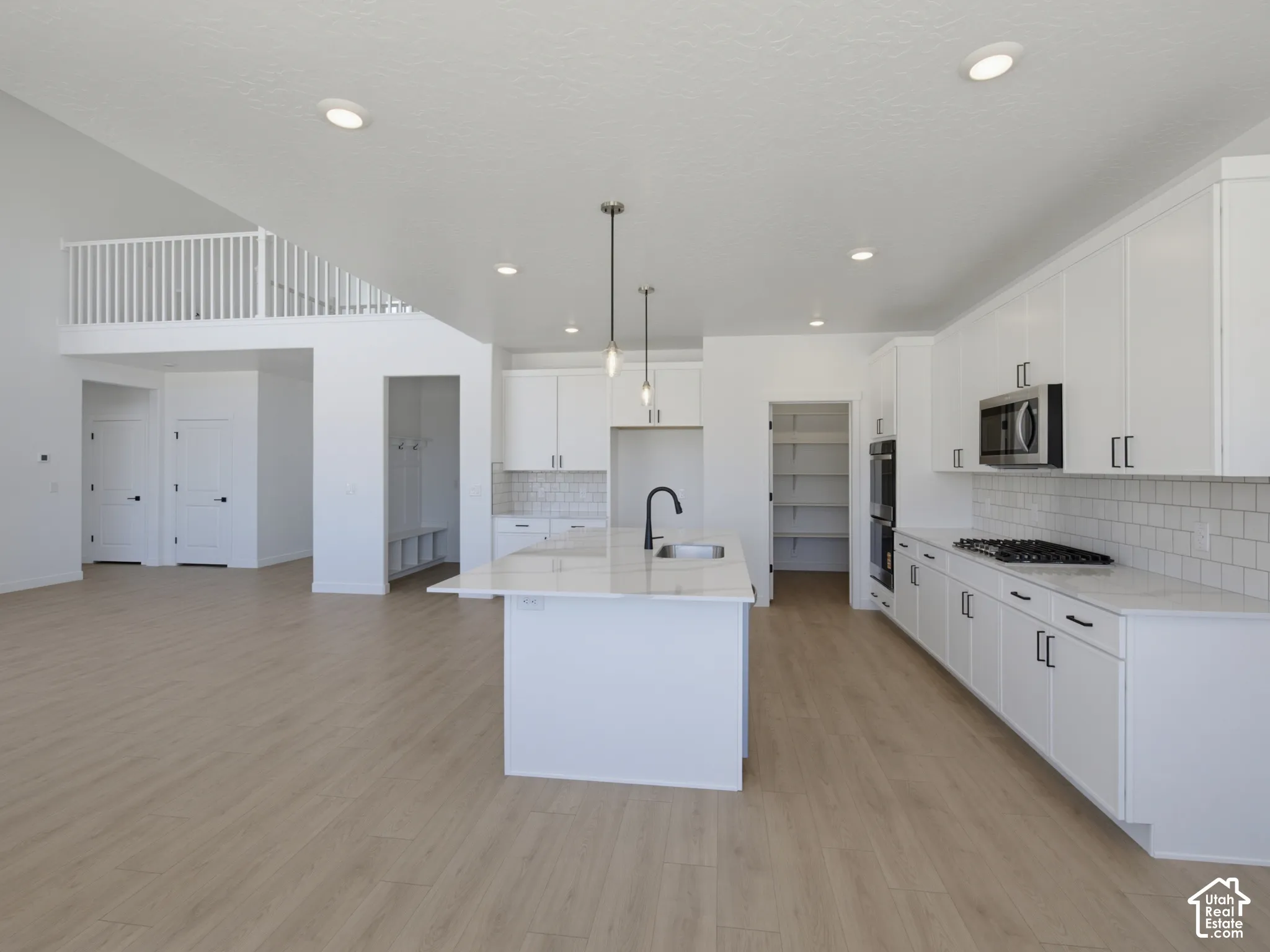 Open-concept living space with wood-finish flooring, a kitchen island with pendant lighting, white cabinetry, integrated stainless steel appliances, and a built-in mudroom area