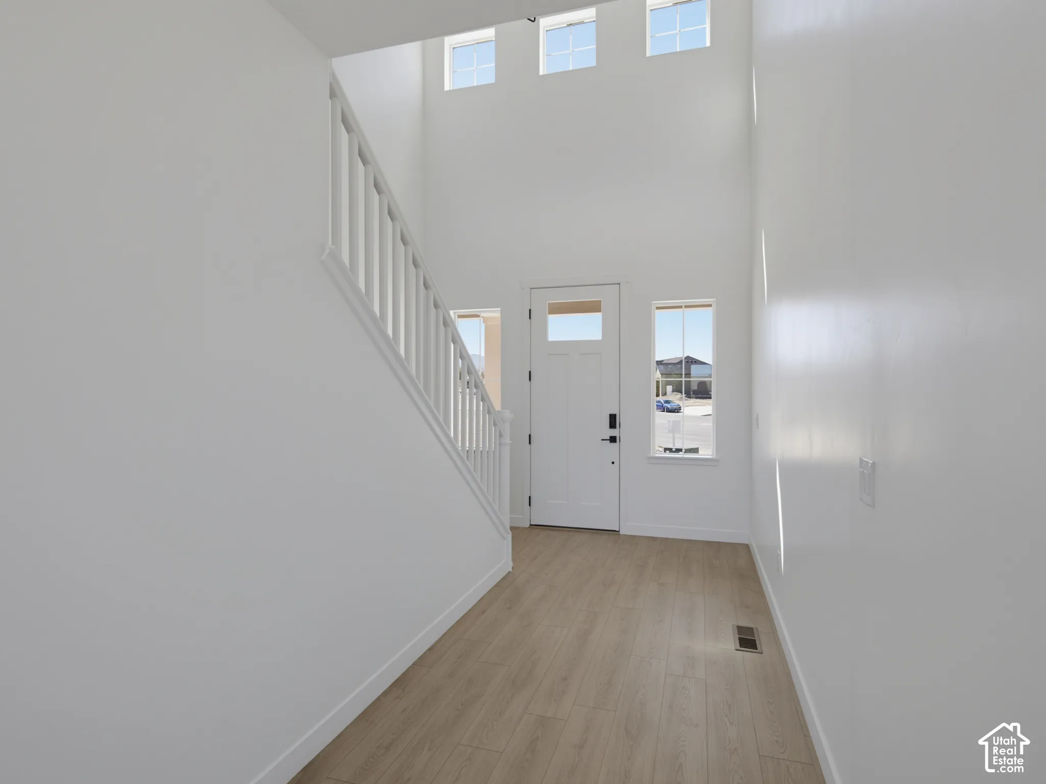 Two-story entry featuring wood-finish flooring, white staircase, and a white entry door with upper glass paneling