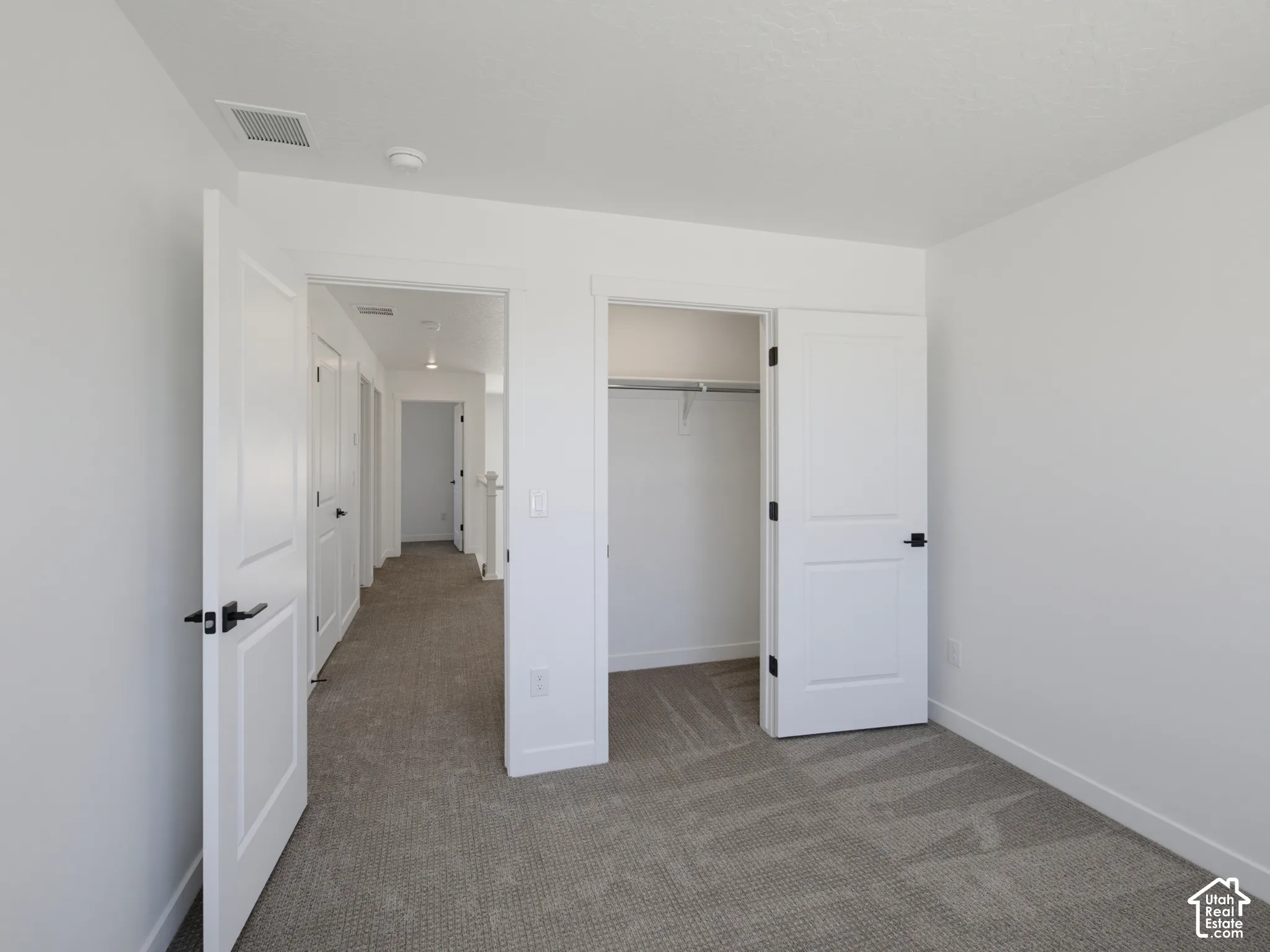 Neutral toned carpeting, white walls, and a closet with a built-in shelf and hanging rod