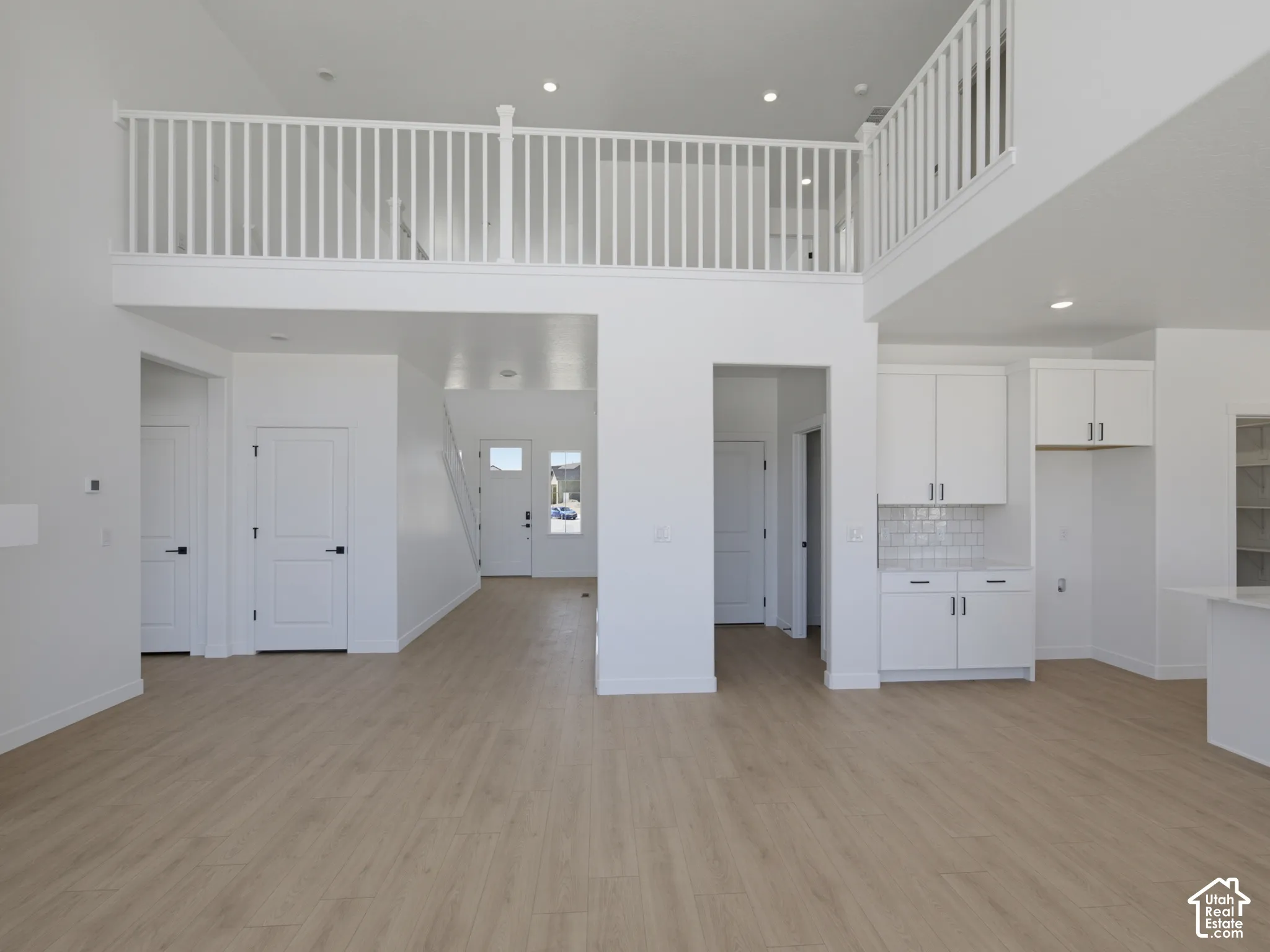 Open-concept space featuring light wood-finish flooring, a white spindle railing balcony, recessed lighting, and white cabinetry with subway tile backsplash