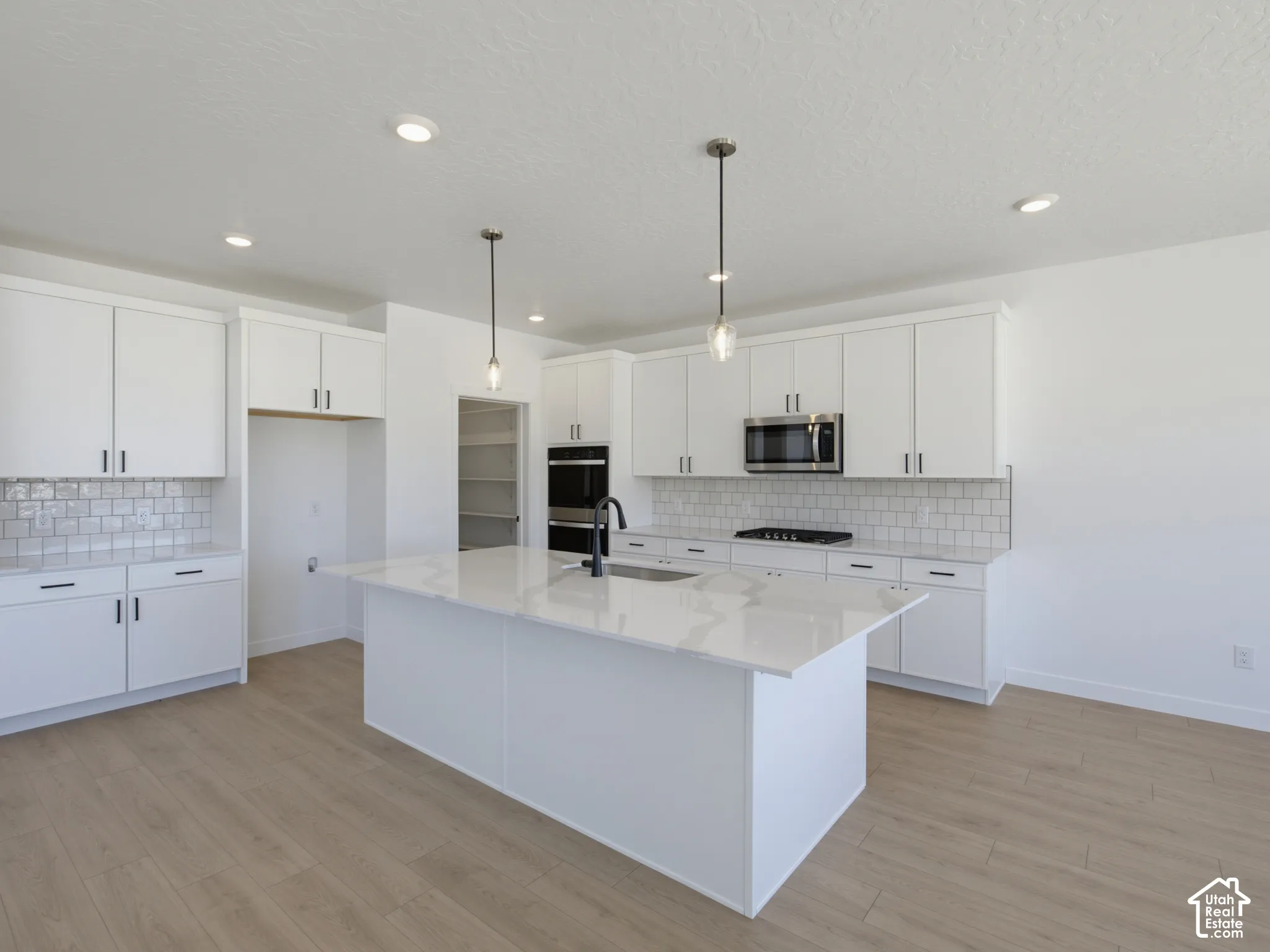 Modern kitchen featuring an expansive center island with countertop, recessed lighting, wood-finish flooring, white cabinetry, and stainless steel appliances