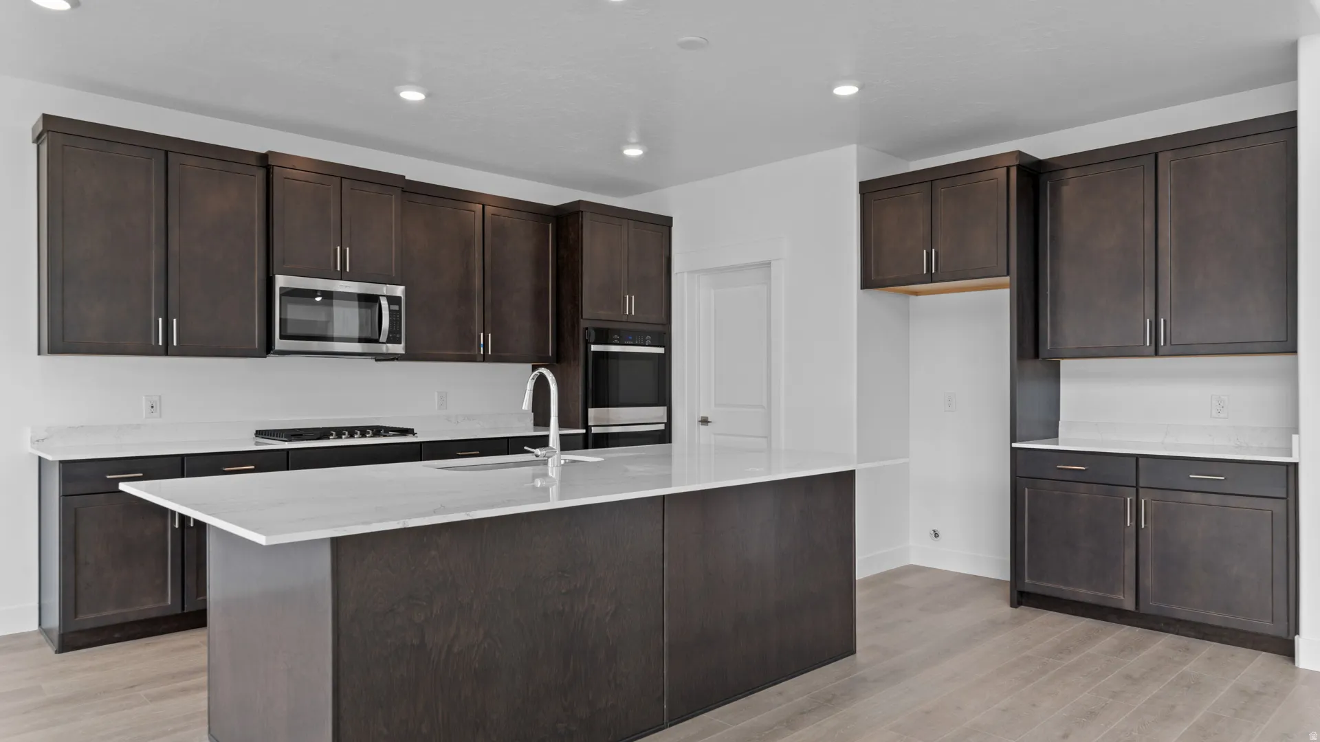 Contemporary kitchen featuring dark wood-finish cabinetry, light stone countertops, and wood-finish flooring