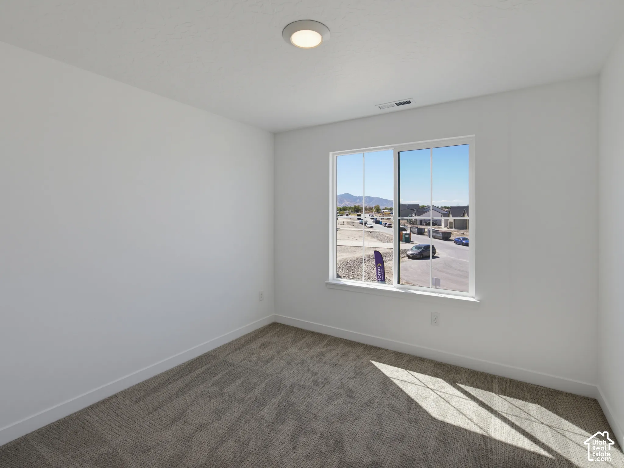 Recessed ceiling light, neutral wall paint, white trim, grey patterned carpet, and a multi-pane window