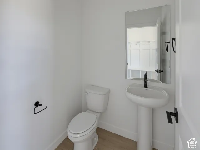 White pedestal sink with a matte black faucet, matching toilet, and wood-finish flooring