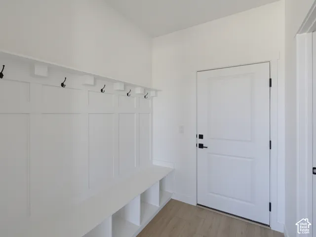 Built-in bench with integrated shelving, wainscoting paneling, multiple coat hooks, white paneled door, and wood-finish flooring