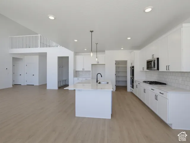 Open-concept living space with wood-finish flooring, a kitchen island with pendant lighting, white cabinetry, integrated stainless steel appliances, and a built-in mudroom area