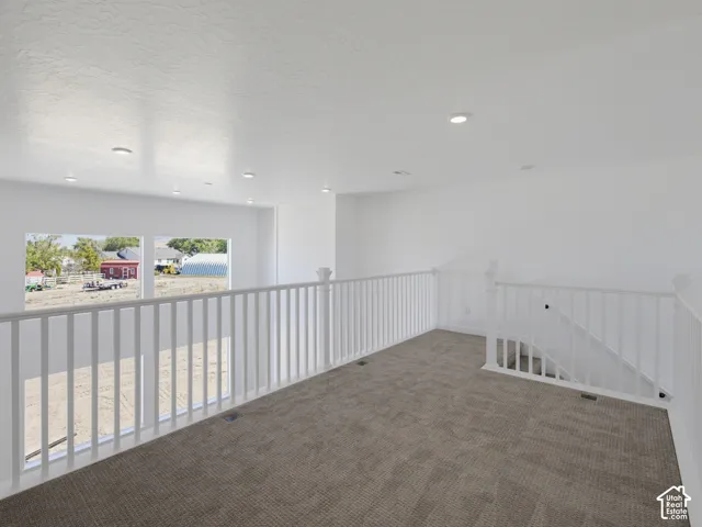 Expansive loft space with gray carpet, white baluster railings, and a series of recessed ceiling lights