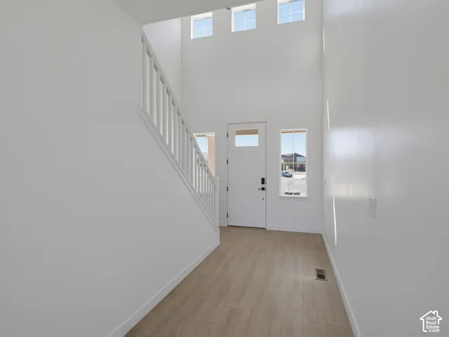 Two-story entry featuring wood-finish flooring, white staircase, and a white entry door with upper glass paneling