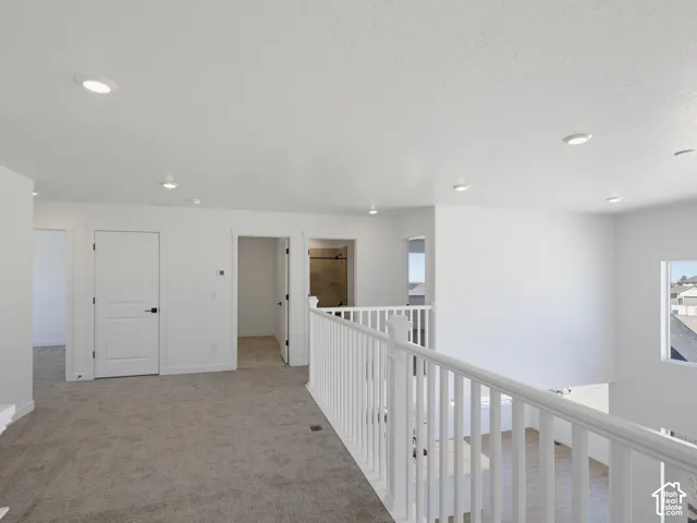 Carpeted landing with white baluster railing, recessed lighting, and multiple interior doors