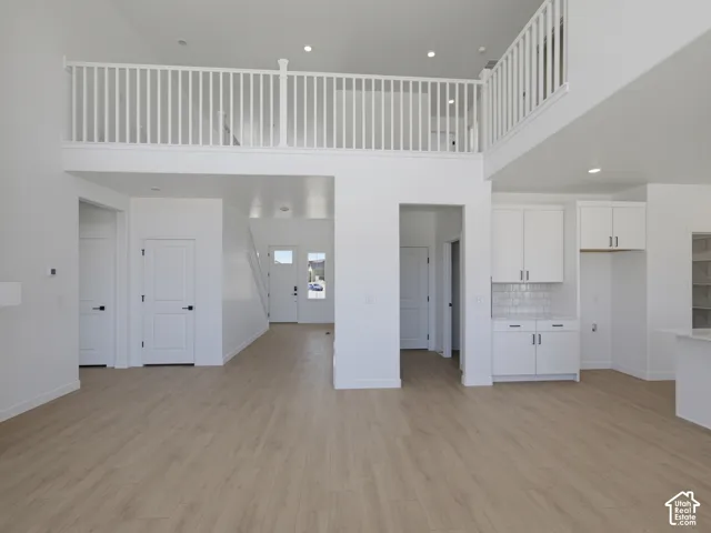 Open-concept space featuring light wood-finish flooring, a white spindle railing balcony, recessed lighting, and white cabinetry with subway tile backsplash