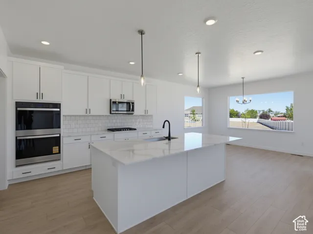 Kitchen featuring white cabinetry, a large central island, stainless steel double wall ovens, a tile backsplash, and light wood-finish flooring
