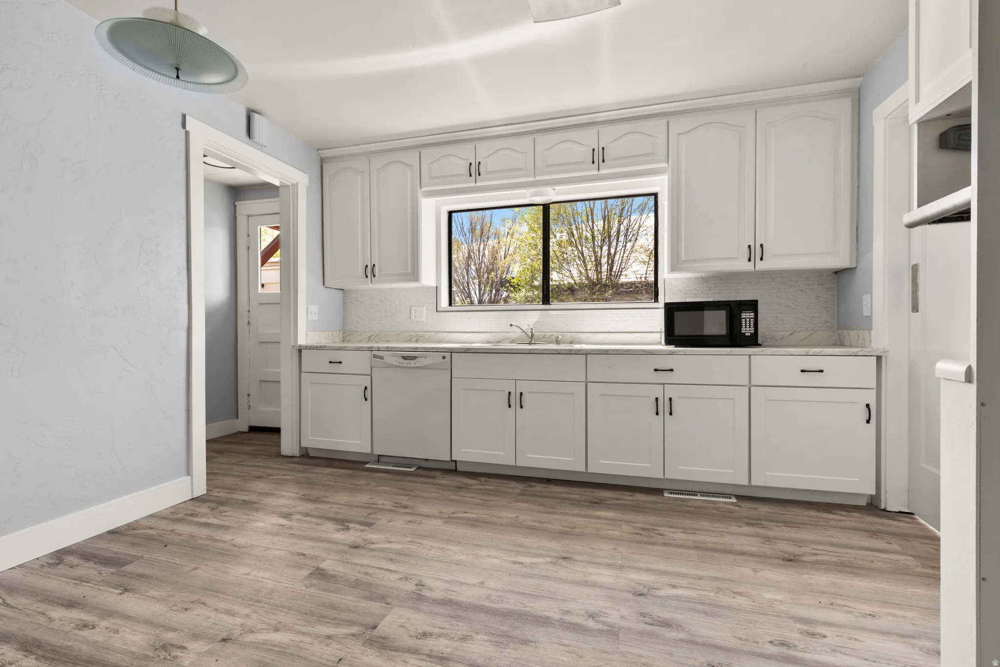 Kitchen with white cabinetry, backsplash, dishwasher, and a textured wall