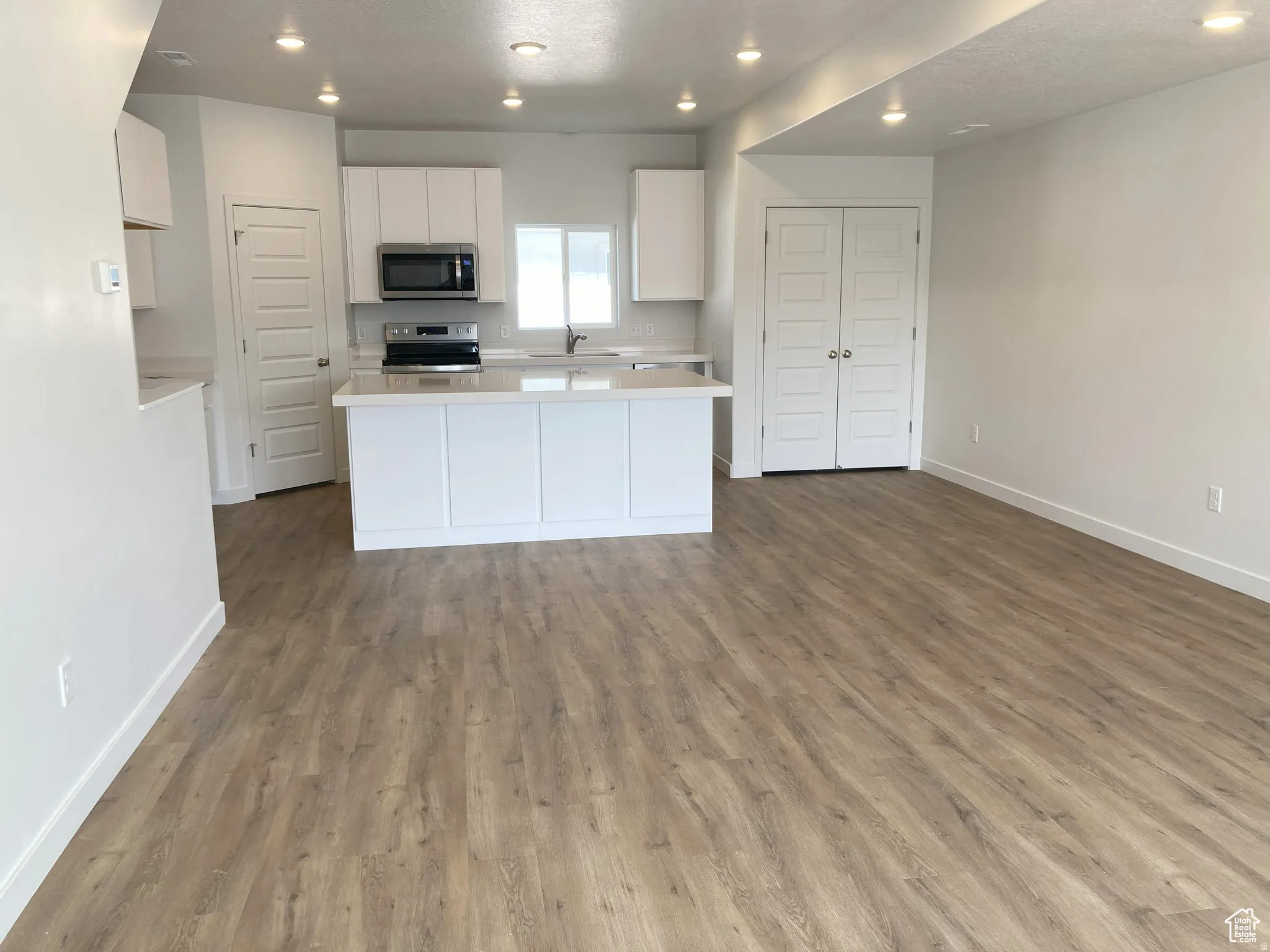 Kitchen with recessed lighting, stainless steel appliances, white cabinets, open floor plan, and dark wood finished floors