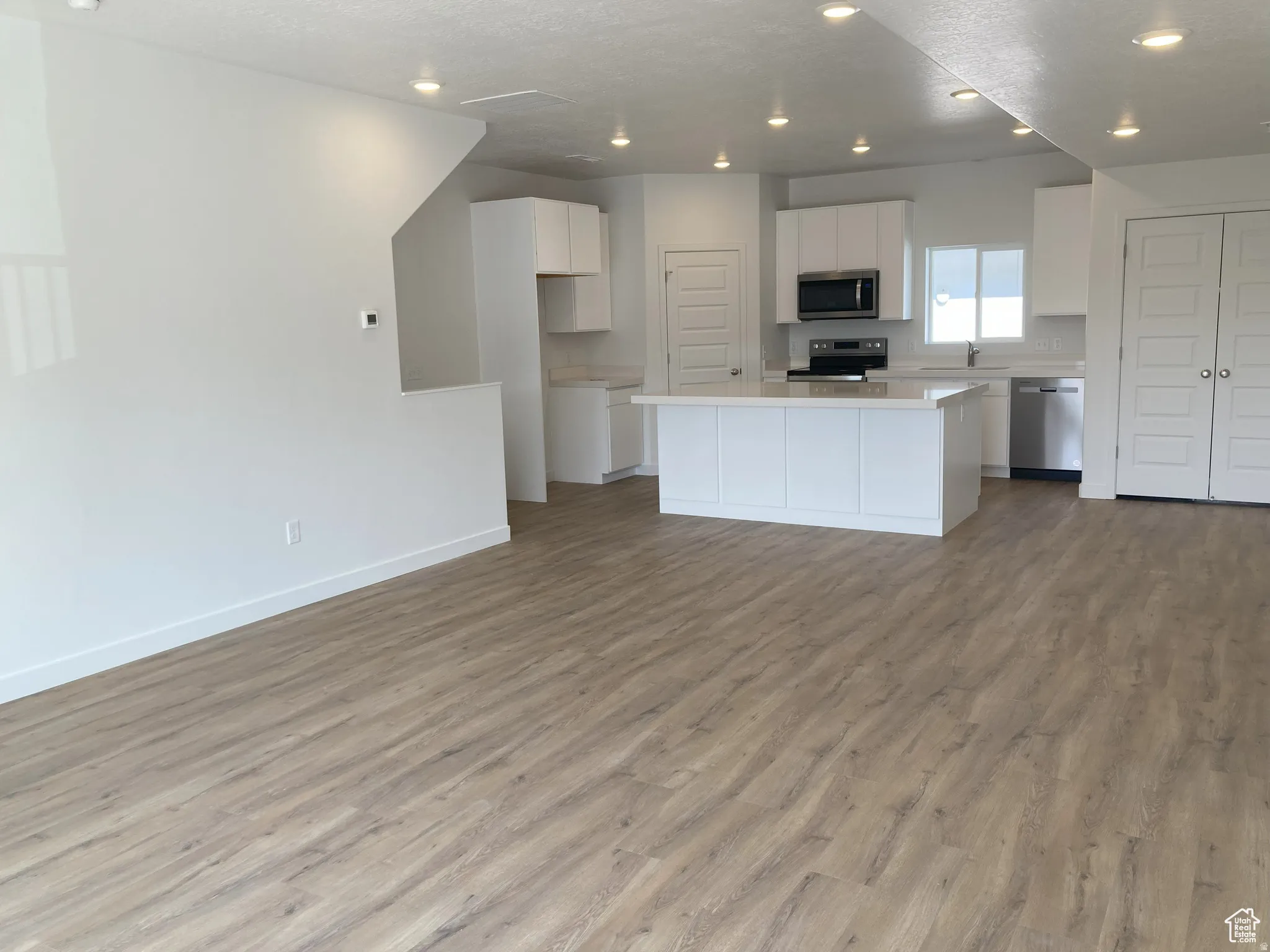 Kitchen with stainless steel appliances, light countertops, white cabinetry, a kitchen island, and open floor plan