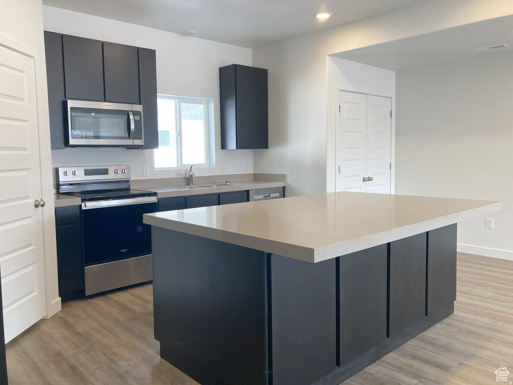 Kitchen featuring stainless steel appliances, a kitchen island, light wood-style flooring, and dark cabinets