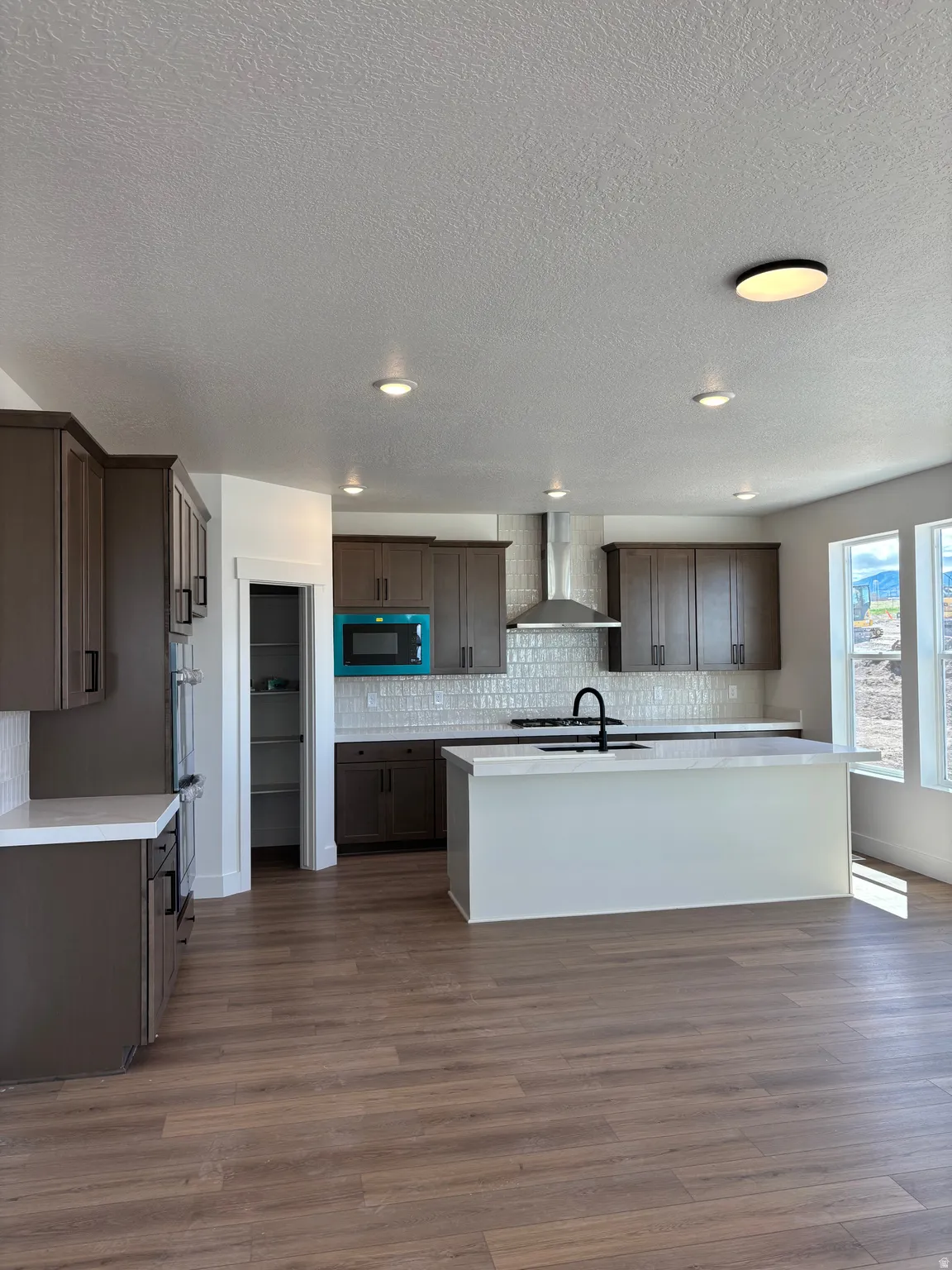 Kitchen with dark wood finish cabinetry, a kitchen island with sink, dark wood-type flooring, built in microwave, and tasteful backsplash