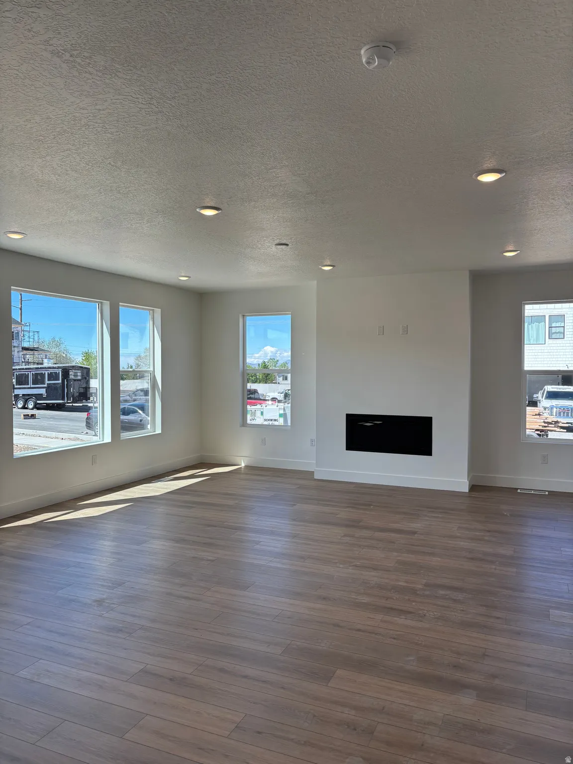 Unfurnished living room with plenty of natural light, recessed lighting, a textured ceiling, dark wood-style flooring, and a fireplace