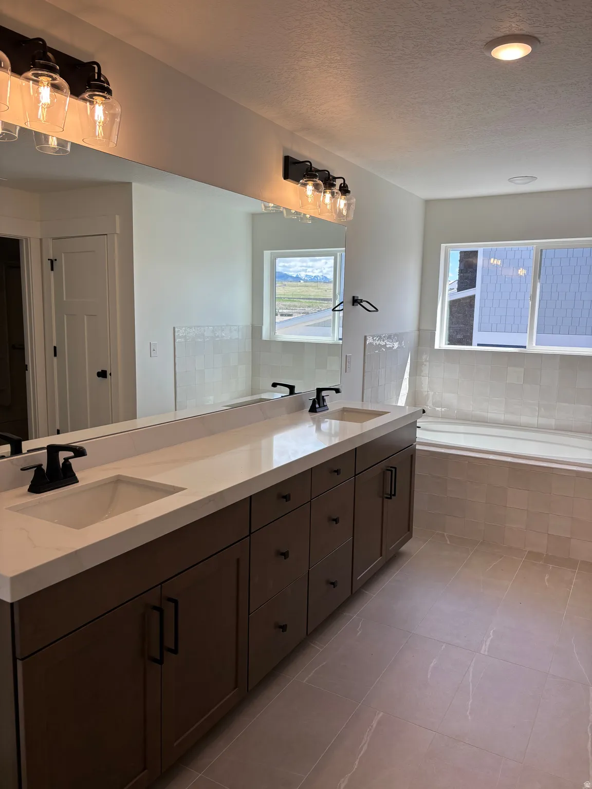 Bathroom with double vanity, a bath, healthy amount of natural light, and a textured ceiling