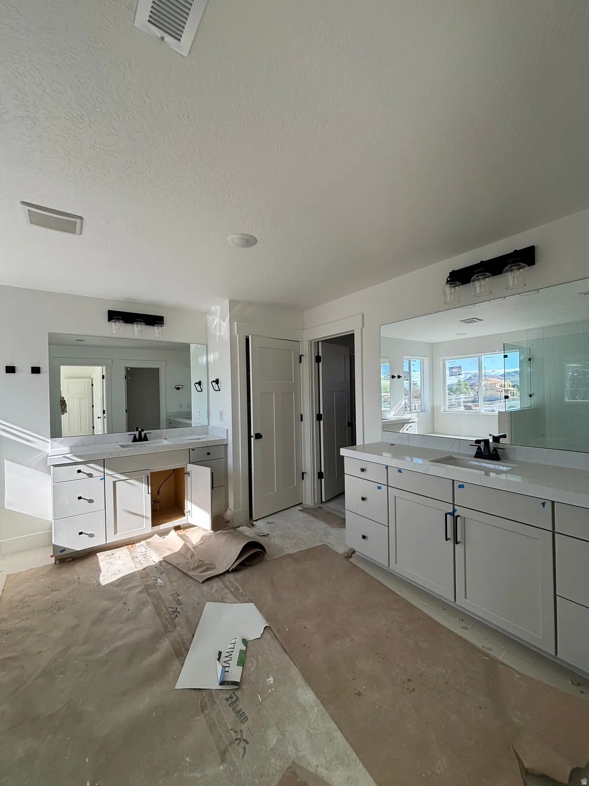 Bathroom featuring two vanities, a textured ceiling, and unfinished concrete flooring