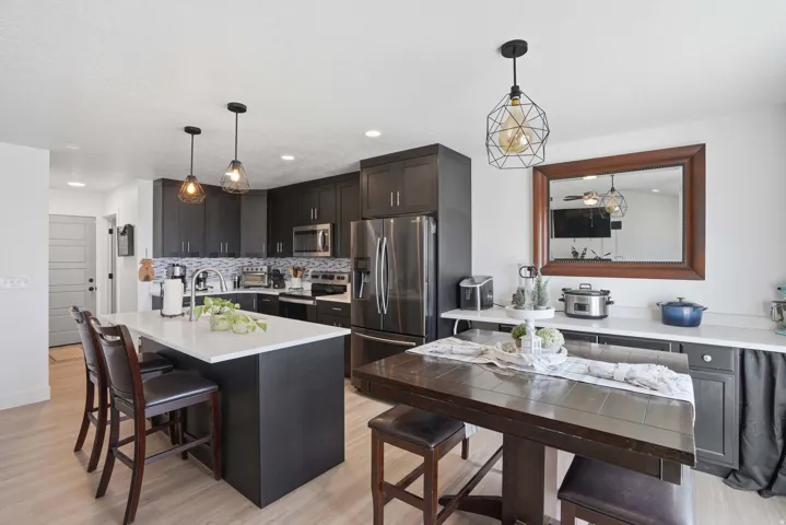 Kitchen featuring stainless steel appliances, a kitchen bar, light wood-style floors, a kitchen island with sink, and pendant lighting