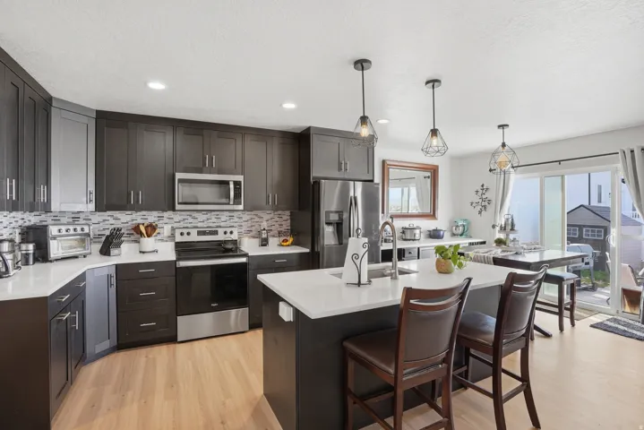 Kitchen with stainless steel appliances, light wood-type flooring, a kitchen breakfast bar, decorative light fixtures, and an island with sink