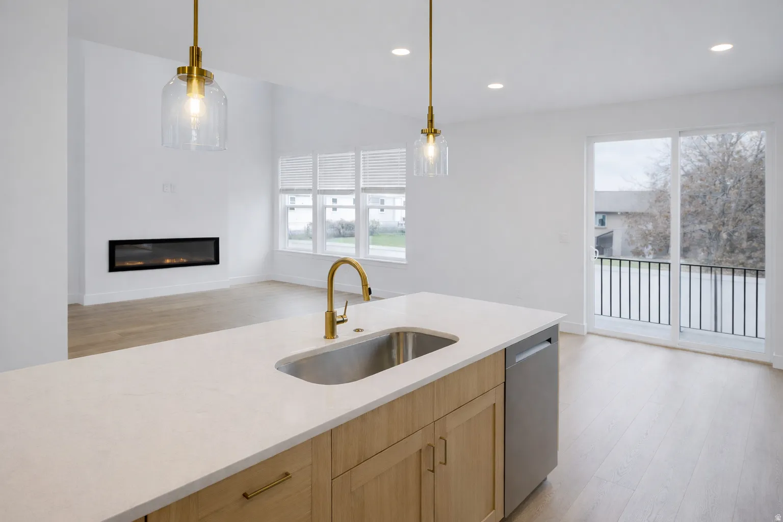 Kitchen with light wood finish cabinetry, light wood-style flooring, a glass covered fireplace, and light stone counters