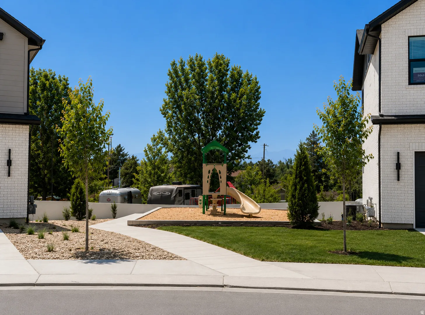 Community green space featuring a playground with a slide, a landscaped rock garden, and a manicured lawn
