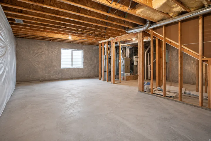 Unfinished basement with exposed ceiling joists, concrete flooring, framed interior walls, and a window with blinds