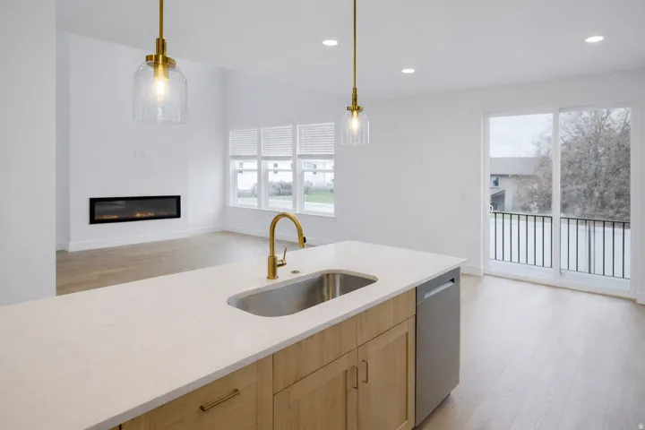 Kitchen with light wood finish cabinetry, light wood-style flooring, a glass covered fireplace, and light stone counters
