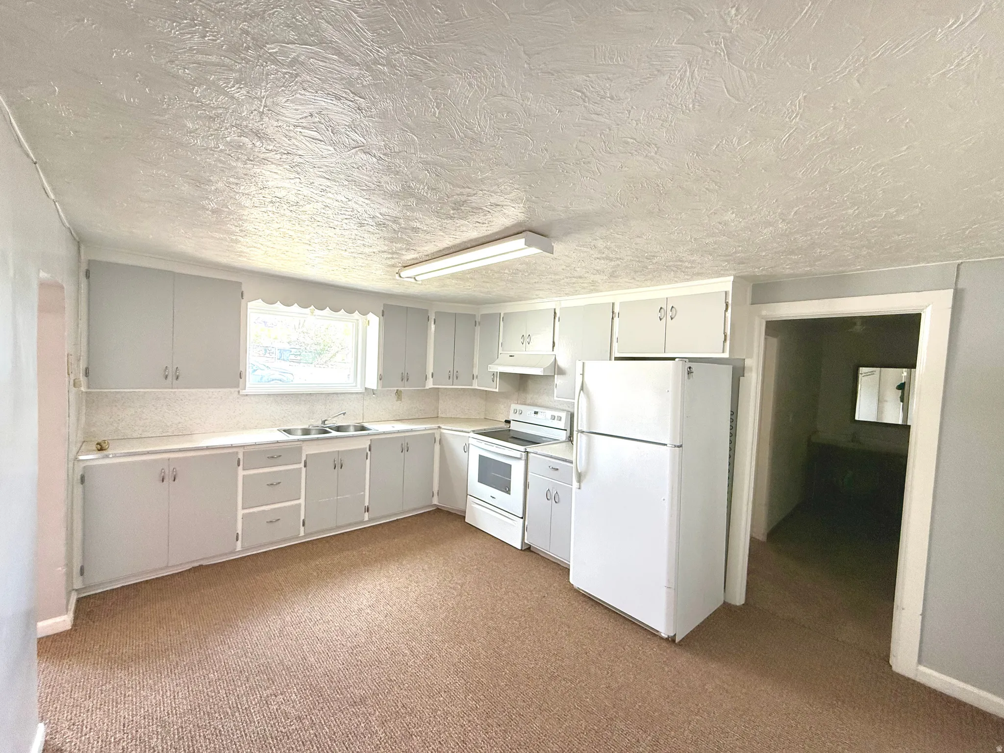 Kitchen with white appliances, light countertops, a textured ceiling, white cabinets, and light colored carpet