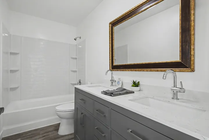 Full bathroom with double vanity, dark wood-type flooring, and shower / washtub combination