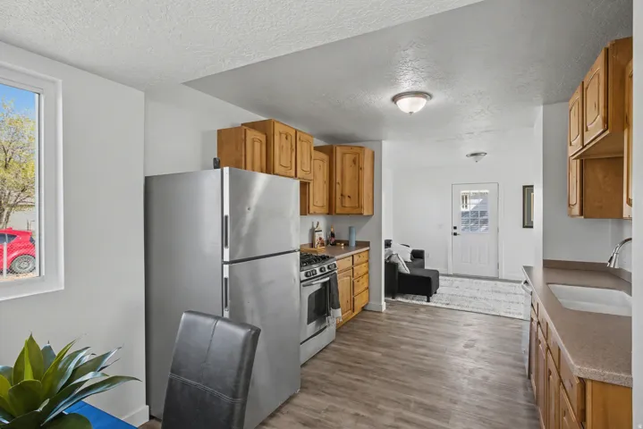 Kitchen with stainless steel appliances, a textured ceiling, wood finish cabinetry, dark wood-style flooring, and dark countertops